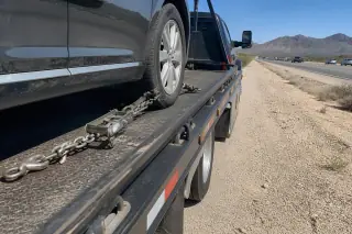 Vehicle secured with heavy-duty chains on a flatbed tow truck on a desert roadside in Phoenix, AZ.