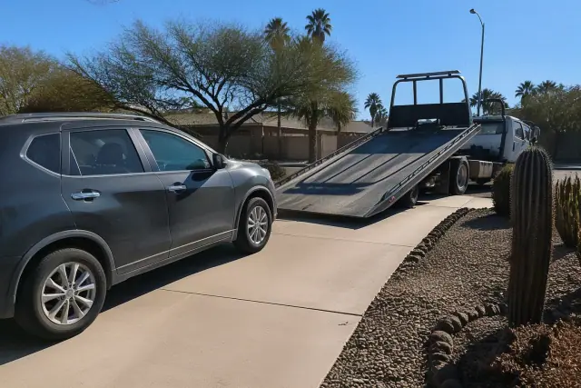 A car parked on a concrete driveway in Phoenix, AZ, ready to be loaded onto a flatbed tow truck.