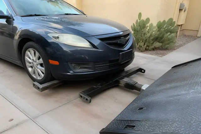 A car being winched onto a flatbed tow truck on a driveway in Phoenix, AZ, with prickly pear cacti and stucco walls.