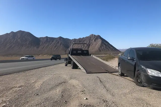 Flatbed tow truck loading a disabled vehicle onto the bed on a desert roadside in Phoenix, AZ.