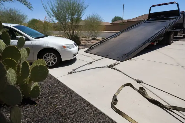 Flatbed tow truck loading a vehicle on a driveway in Chandler, AZ with desert landscaping.