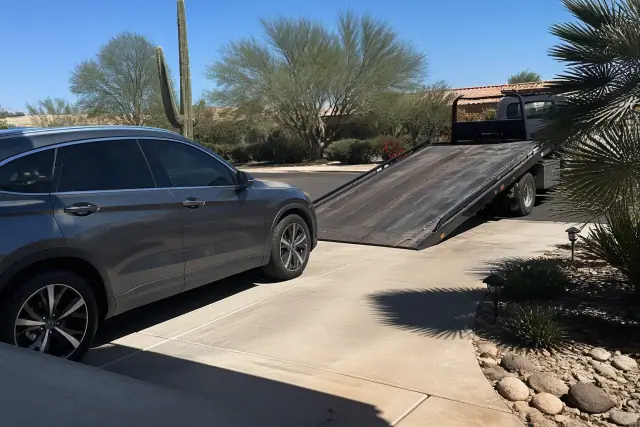 A vehicle on a residential driveway in Scottsdale, AZ, being prepared for loading onto a flatbed tow truck.