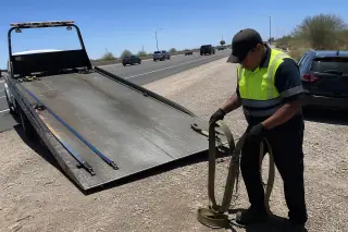 Contractor coiling tie-down straps on a flatbed tow truck on a highway shoulder in Phoenix, AZ.