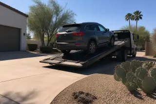 Vehicle secured on a flatbed tow truck on a concrete driveway near prickly pear cacti in Phoenix, AZ.