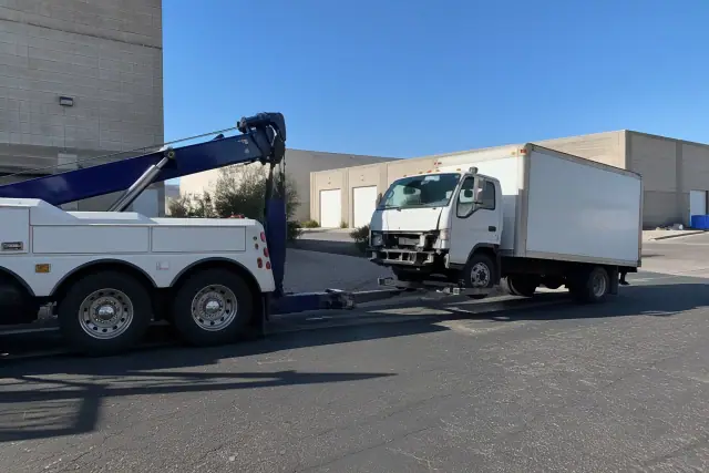 Heavy-duty wrecker towing a damaged box truck at an industrial warehouse in Phoenix, AZ.