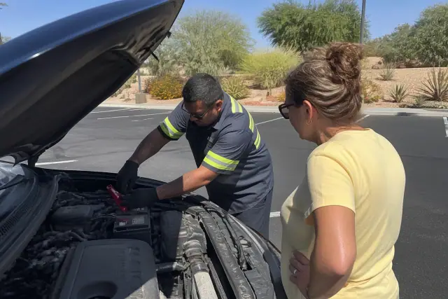 Technician using jumper cables on a car battery in a Scottsdale, AZ parking lot.