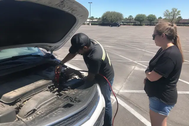 A technician using jumper cables on a vehicle battery in a parking lot in Mesa, AZ.
