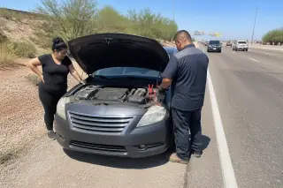 Technician disconnecting jump-start cables from a car on a gravel highway shoulder in Phoenix, AZ.