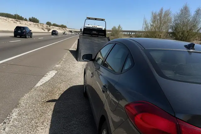 A disabled car parked on a gravel highway shoulder during a sunny day in Phoenix, AZ.