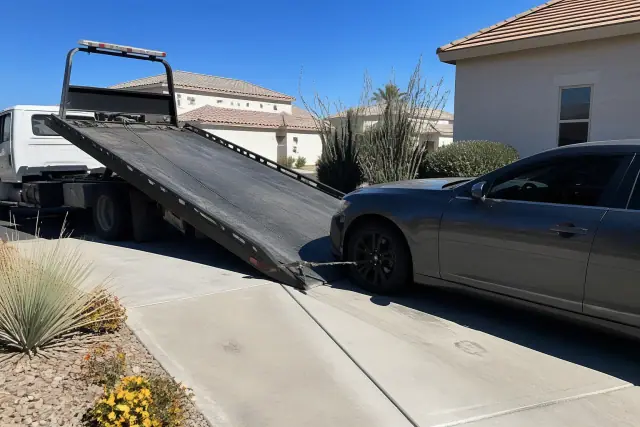 A tow truck winching a vehicle onto a hydraulic bed in a residential driveway in Surprise, AZ.