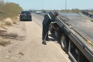 Technician sweeping road debris and checking tire straps on a tow truck in Phoenix, AZ.