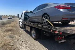 Disabled vehicle secured with wheel straps on a tow truck flatbed on a dusty Phoenix, AZ highway shoulder.