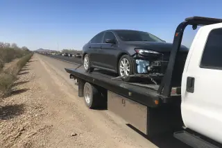 Vehicle secured on a flatbed tow truck parked on a desert highway shoulder in Phoenix, AZ.