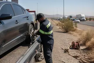 Tow truck operator checking a secured vehicle on a gravel highway shoulder in Phoenix, AZ with desert scrub background.