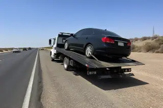 Disabled vehicle secured on a flatbed tow truck on a sun-bleached desert highway shoulder in Phoenix, AZ.