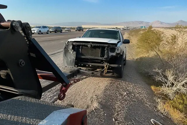 A heavy-duty tow truck hitched to a disabled vehicle on a gravel shoulder in Phoenix, AZ.