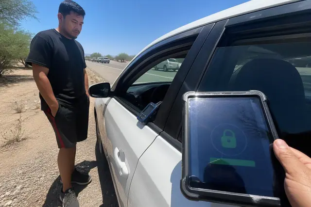 Technician using a tablet to unlock a car parked on the shoulder of a road in Phoenix, AZ.