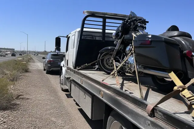 Motorcycle secured on a flatbed tow truck on a highway shoulder in Phoenix, AZ.
