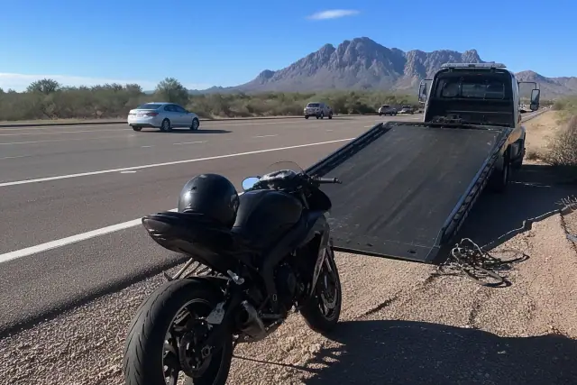 A disabled motorcycle parked on a gravel highway shoulder with desert mountains in the background in Phoenix, AZ.