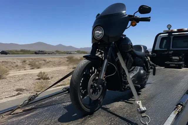 A motorcycle secured to a flatbed tow truck on a highway shoulder in Mesa, AZ, with desert scenery in the background.