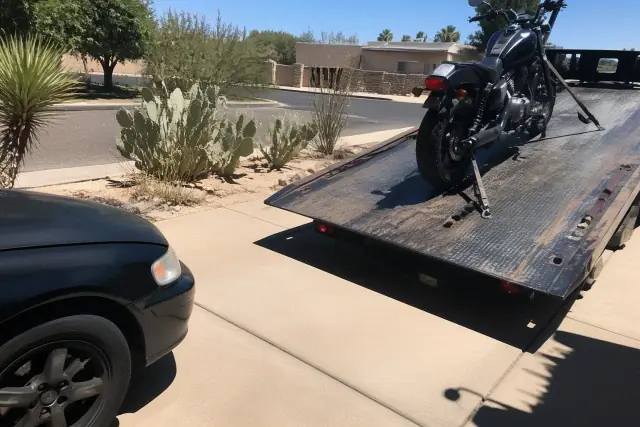 A motorcycle secured with tie-downs on a tow truck bed in a residential driveway in Phoenix, AZ.
