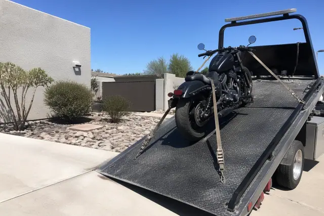 Motorcycle secured with tie-downs on a tow truck bed in a private driveway in Tempe, AZ.