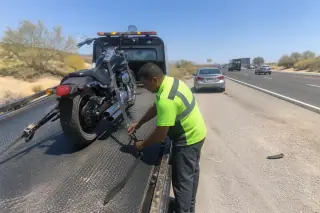 Contractor inspecting straps on a motorcycle secured to a tow truck on a Phoenix, AZ highway shoulder.