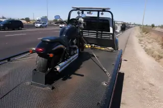 Motorcycle secured with ratchet straps and wheel chocks on a flatbed tow truck on a desert highway in Phoenix, AZ.