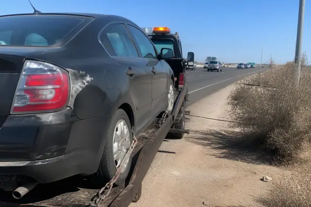 Disabled vehicle secured to a tow truck on a highway shoulder in Phoenix, AZ.