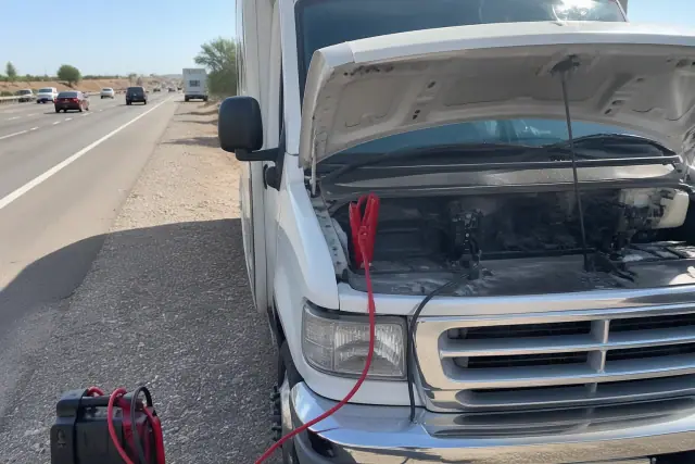 Jumper cables connected to dual battery banks under the open hood of a vehicle on a roadside in Phoenix, AZ.