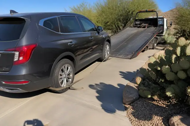 A vehicle being loaded onto a tow truck in a residential driveway with desert landscaping in Phoenix, AZ.