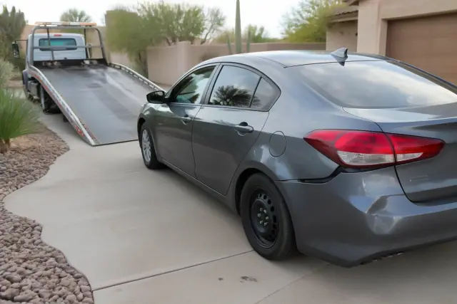 Damaged car on a residential driveway in Phoenix, AZ, prepared for loading onto a tow truck.