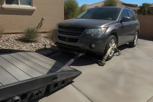 Vehicle being secured with winch hooks and wheel straps for towing on a concrete driveway in Phoenix, AZ.