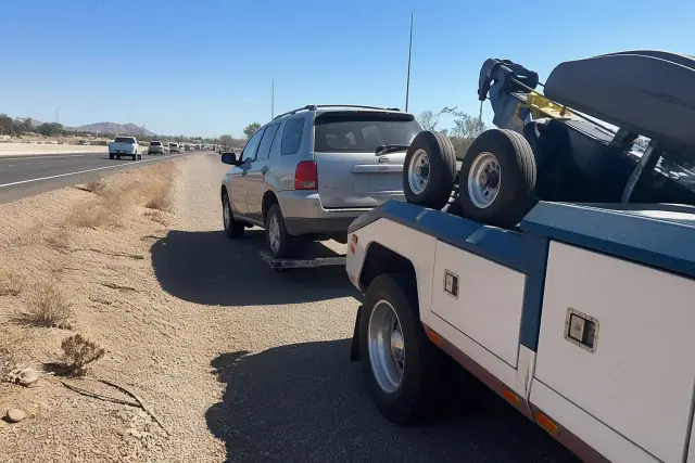 Wheel-lift tow truck recovering a disabled vehicle on a highway shoulder in Phoenix, AZ.