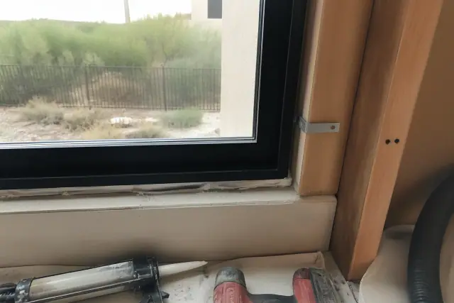 Aluminum window frame installation at a residential home in Queen Creek, AZ with tools and sealant visible on a drop cloth.