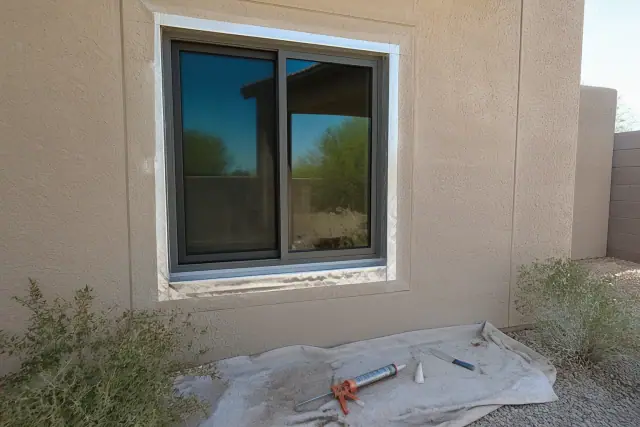 Aluminum window installation with a caulking gun and flashing tape on a stucco wall at a job site in Peoria, AZ.