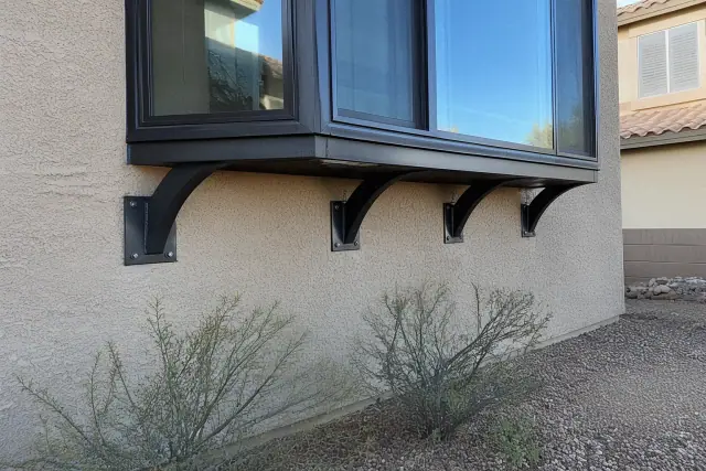 Heavy-duty steel support brackets installed beneath a bay window on a stucco wall in Surprise, AZ.