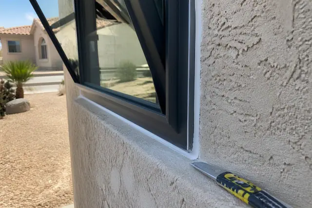 Freshly applied caulk sealing a new window frame on a stucco wall in Peoria, AZ.