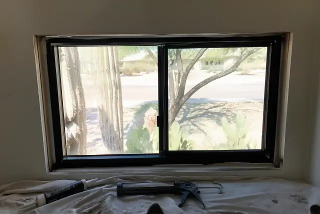 Newly installed window frame with a caulking gun and sealant on a drop cloth at a job site in Peoria, AZ.