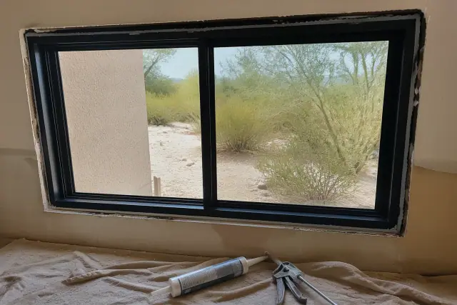 A window frame installed in a stucco wall with a caulk gun and sealant on a drop cloth in Queen Creek, AZ.