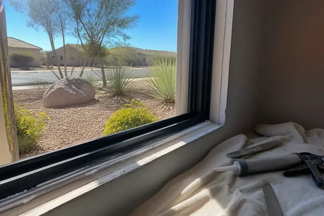 A new window frame installed in a wall with fresh sealant and tools on a drop cloth in a home in Surprise, AZ.