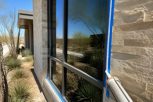 Worker caulking the frame of a new commercial window in Phoenix, AZ, with desert landscaping in the background.