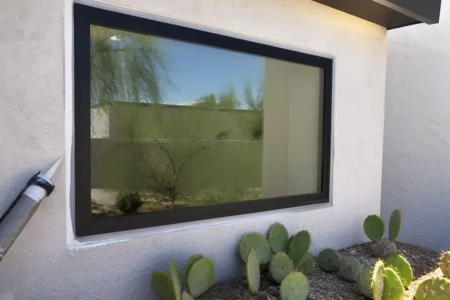 Caulk being applied to a custom aluminum window frame on a stucco wall in Phoenix, AZ with desert landscaping.