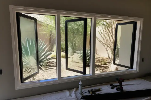 Custom casement and awning window frame installation in a Phoenix, AZ home with desert landscaping visible outside.