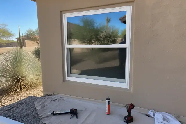 Double-hung window frame installed in a stucco wall with construction tools on a drop cloth in Phoenix, AZ.