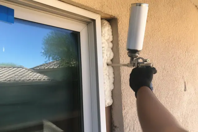 Contractor applying insulating foam between a window frame and stucco wall at a job site in Phoenix, AZ.