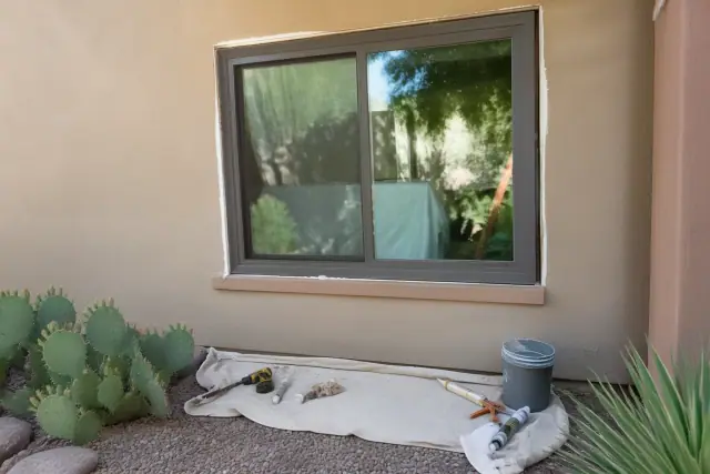 A newly installed window frame with tools on a drop cloth and desert landscaping at a residential job site in Glendale, AZ.