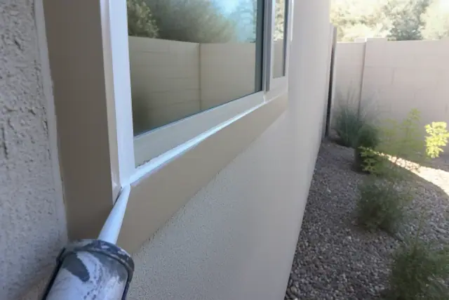 A technician applying caulk to a window frame on a stucco house in Phoenix, AZ.