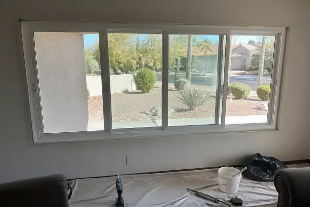 Multi-chamber vinyl window frame installation in a Phoenix, AZ residential living room with tools on a drop cloth.
