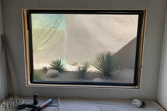 A picture window frame being installed in a wall in Phoenix, AZ, with tools and materials on a drop cloth.